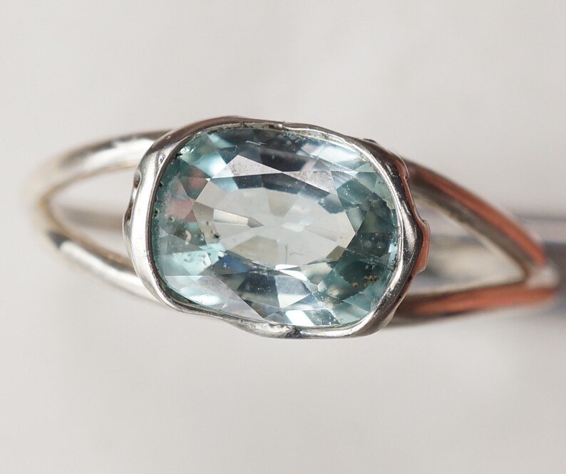 May include: A silver ring with a light blue oval gemstone set in a bezel setting.