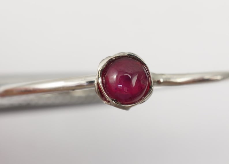 K&ouml;nnte beinhalten: Ein silberner Ring mit einem tief roten Edelstein, der in einem zarten, gedrehten Band gefasst ist.