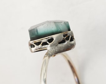 May include: A silver ring with a green and white gemstone set in a silver and gold setting.