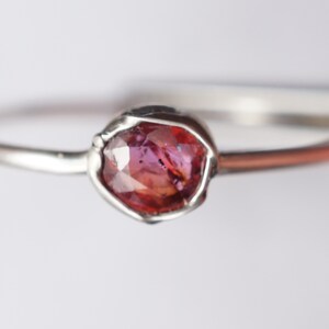 Op de afbeelding: Een zilveren ring met een roze edelsteen in een bezel-setting.