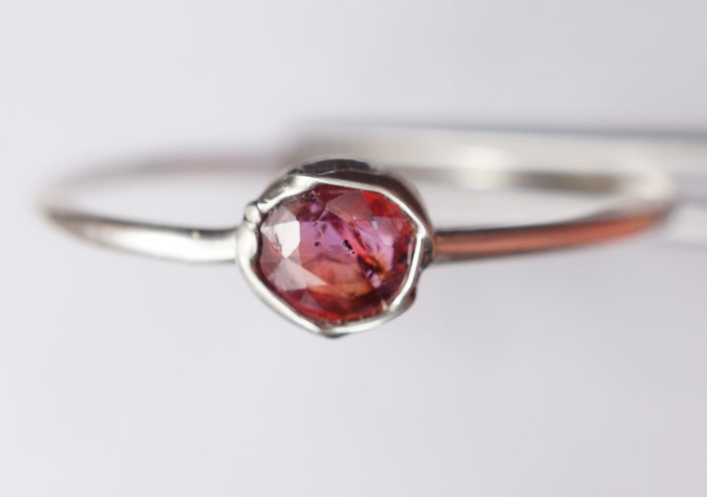 Op de afbeelding: Een zilveren ring met een roze edelsteen in een bezel-setting.