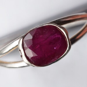 Op de afbeelding: Een zilveren ring met een grote, diep rode, gefacetteerde edelsteen in een bezel-setting.