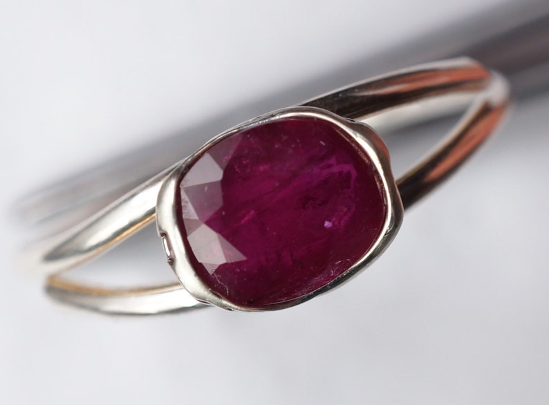 Op de afbeelding: Een zilveren ring met een grote, diep rode, gefacetteerde edelsteen in een bezel-setting.