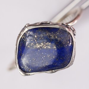 Puede incluir: Un anillo de plata con una gran piedra de lapisl&aacute;zuli azul engastada en un engaste de plata texturizado. La piedra tiene un aspecto moteado con motas doradas.