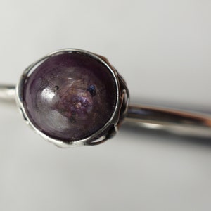 May include: A silver ring with a purple gemstone set in a wire cage. The gemstone is round and has a slightly cloudy appearance.