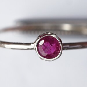 May include: A silver ring with a small, round, pink ruby gemstone.