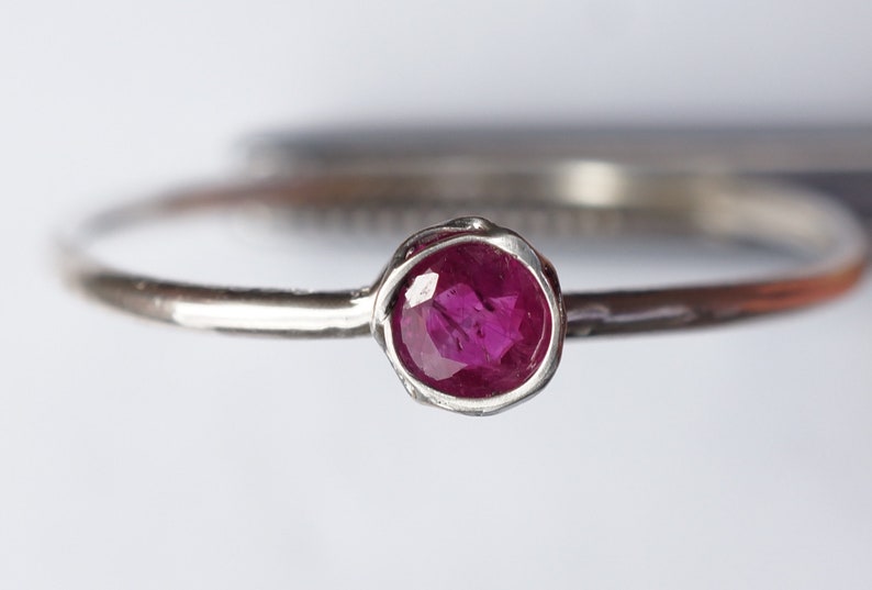 May include: A silver ring with a small, round, pink ruby gemstone.