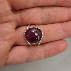 May include: A silver ring with a deep red cabochon gemstone set in a bezel setting.