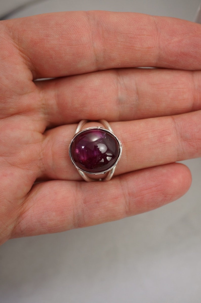 May include: A silver ring with a deep red cabochon gemstone set in a bezel setting.