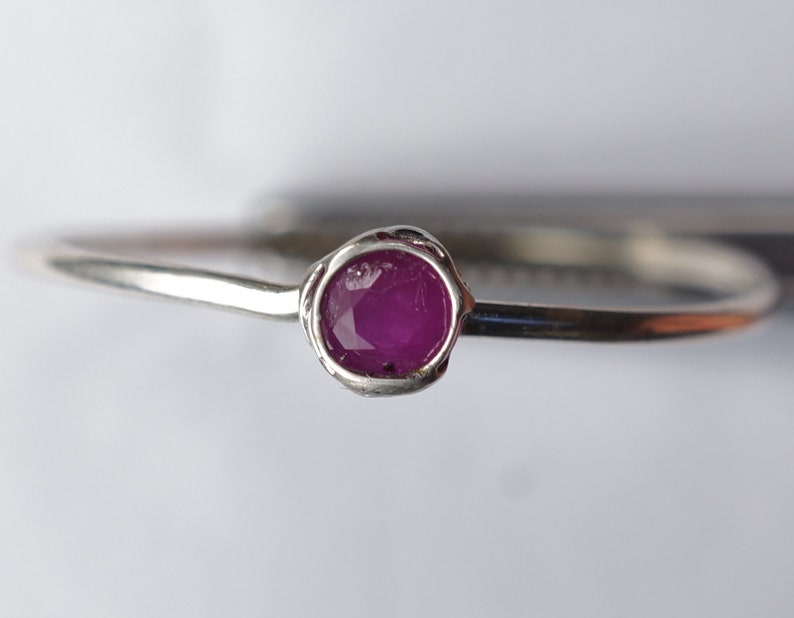 K&ouml;nnte beinhalten: Ein silberner Ring mit einem einzigen, runden, rosafarbenen Rubin, der in der Mitte eingesetzt ist.
