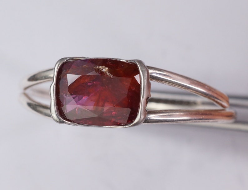Pu&ograve; includere: Un anello d'argento con una pietra preziosa sfaccettata di colore rosso scuro incastonata in una montatura a castone.