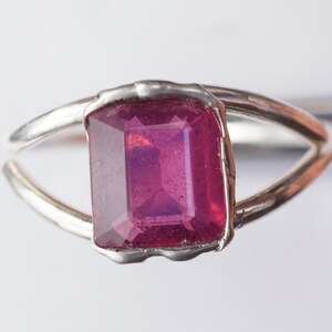 May include: A silver ring with a deep pink, emerald-cut gemstone.