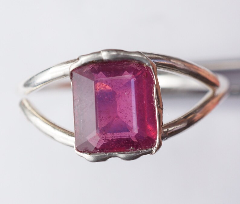 May include: A silver ring with a deep pink, emerald-cut gemstone.