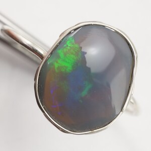 May include: A silver ring with a large, oval-shaped black opal gemstone. The opal has a green, blue, and purple iridescence.