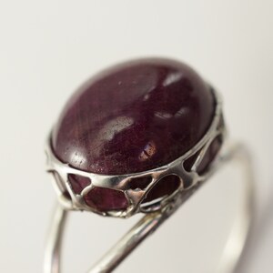 Pu&ograve; includere: Un anello d'argento con una grande pietra preziosa ovale di colore viola scuro incastonata in un delicato design traforato.