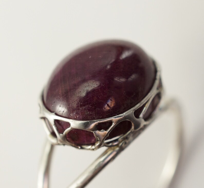 Pu&ograve; includere: Un anello d'argento con una grande pietra preziosa ovale di colore viola scuro incastonata in un delicato design traforato.