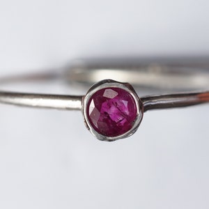 May include: A silver ring with a small, round, pink ruby gemstone set in a textured band.