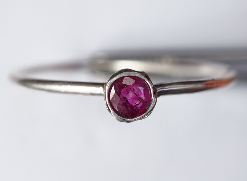 May include: A silver ring with a small, round, pink ruby gemstone set in a textured band.