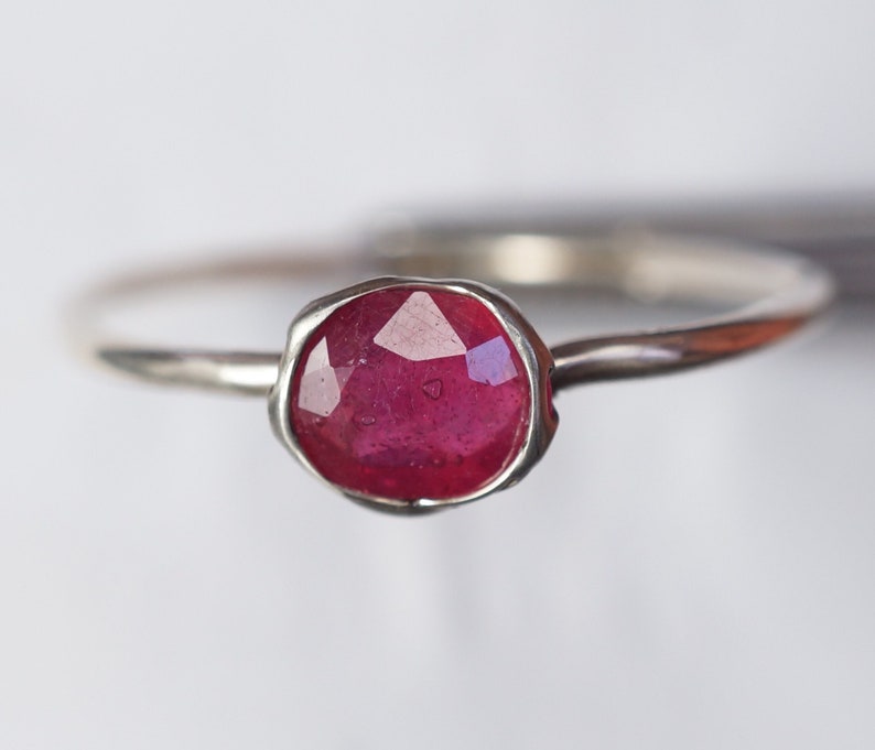 May include: A silver ring featuring a red ruby gemstone. The ruby is faceted and has a slightly irregular shape.