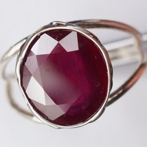 May include: A silver ring with a large, faceted ruby gemstone. The ruby is a deep red color and has a high polish.