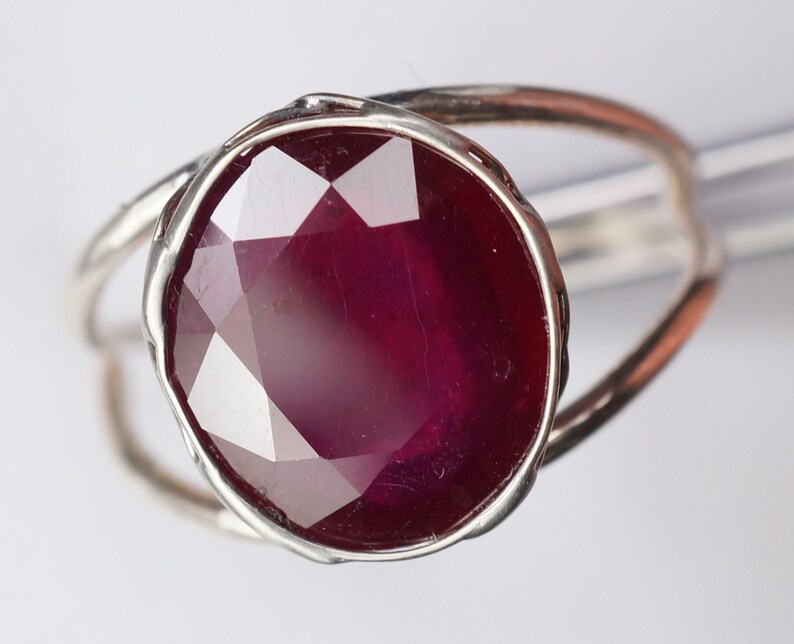 May include: A silver ring with a large, faceted ruby gemstone. The ruby is a deep red color and has a high polish.