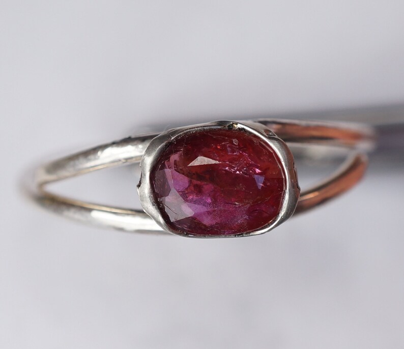 Puede incluir: Un anillo de plata con una piedra ovalada rosa engastada en un engaste de bisel.