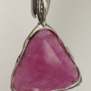 May include: A silver pendant featuring a triangular pink gemstone set in a wire frame.