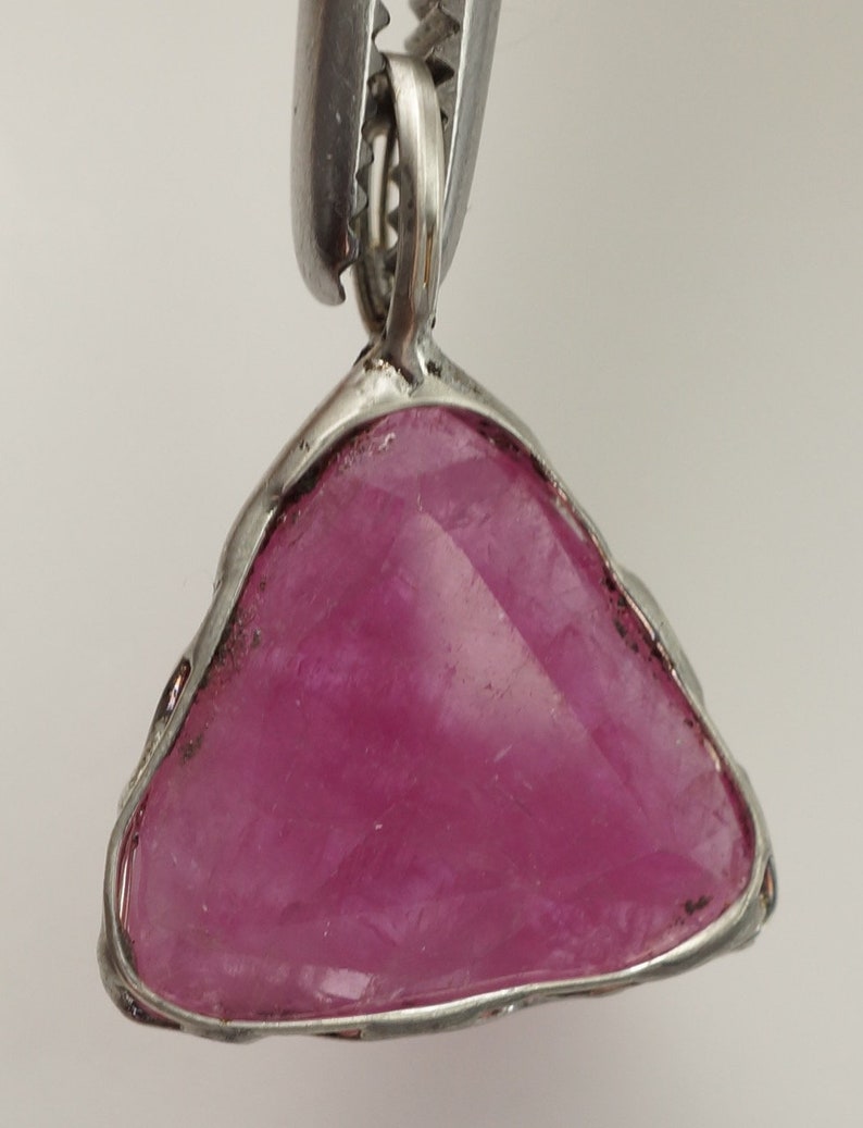 May include: A silver pendant featuring a triangular pink gemstone set in a wire frame.