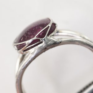 May include: A silver ring with a large, oval-shaped, dark purple gemstone set in a delicate, wire-like frame.