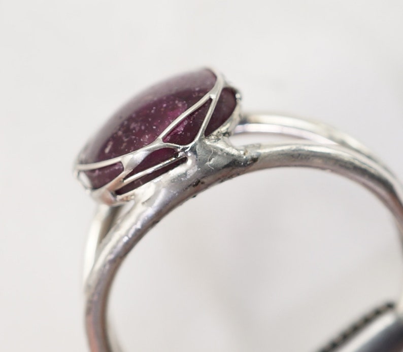May include: A silver ring with a large, oval-shaped, dark purple gemstone set in a delicate, wire-like frame.