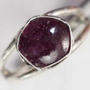 May include: A silver ring with a deep purple gemstone set in a rough, textured bezel.