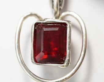 May include: A silver pendant featuring a red gemstone set within a heart-shaped frame.