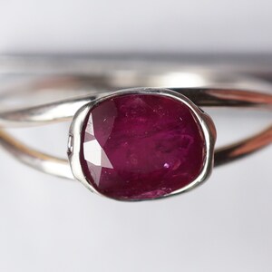 Op de afbeelding: Een zilveren ring met een dieprode edelsteen in een bezel-setting. De ring heeft een eenvoudig, elegant ontwerp.