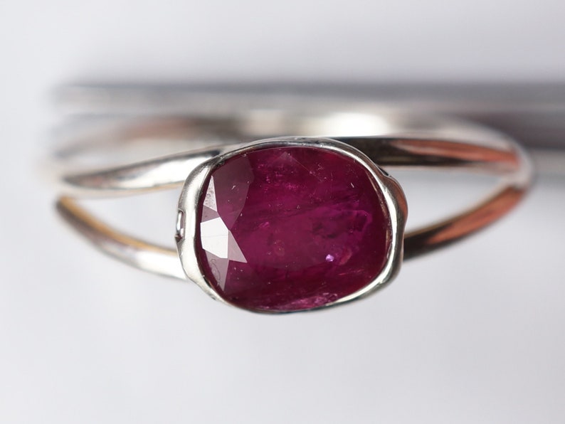 Op de afbeelding: Een zilveren ring met een dieprode edelsteen in een bezel-setting. De ring heeft een eenvoudig, elegant ontwerp.