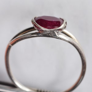 Op de afbeelding: Een zilveren ring met een rode robijn-edelsteen gezet in een delicaat, ingewikkeld ontwerp.