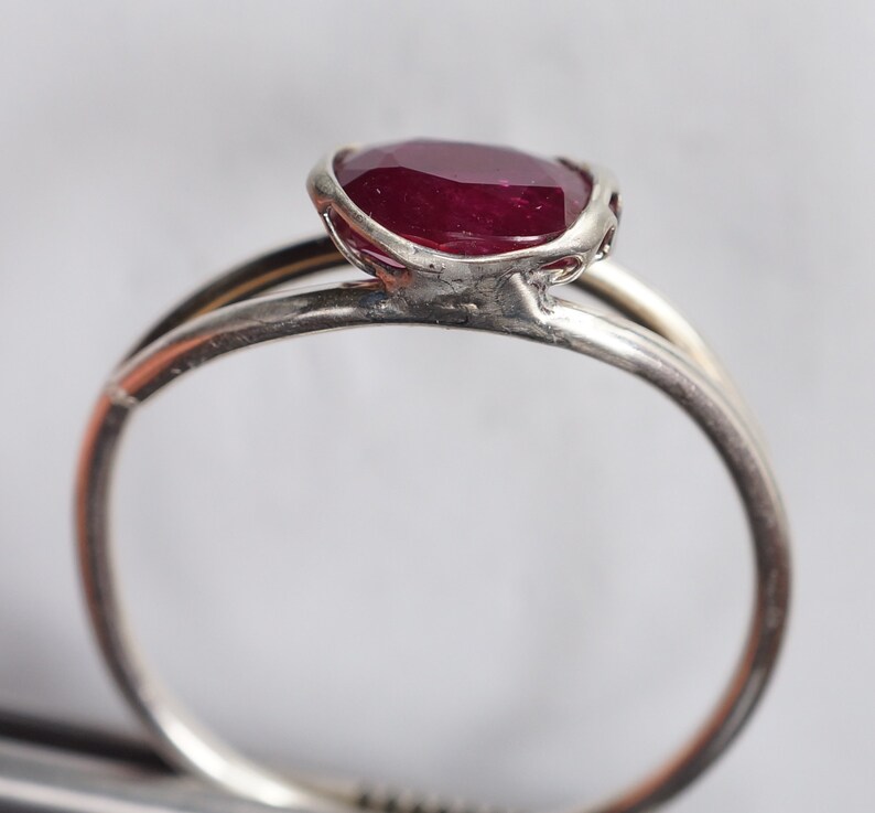 Op de afbeelding: Een zilveren ring met een rode robijn-edelsteen gezet in een delicaat, ingewikkeld ontwerp.