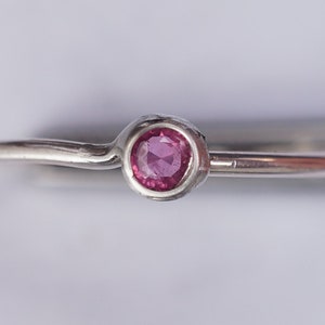 K&ouml;nnte beinhalten: Ein silberner Ring mit einem kleinen, runden, rosafarbenen Edelstein in der Mitte.