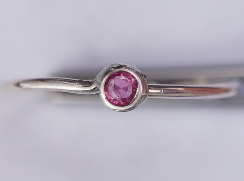 K&ouml;nnte beinhalten: Ein silberner Ring mit einem kleinen, runden, rosafarbenen Edelstein in der Mitte.