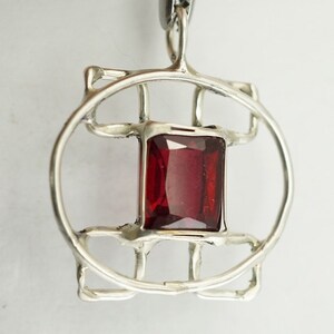 May include: A silver pendant featuring a red gemstone set within a geometric design.