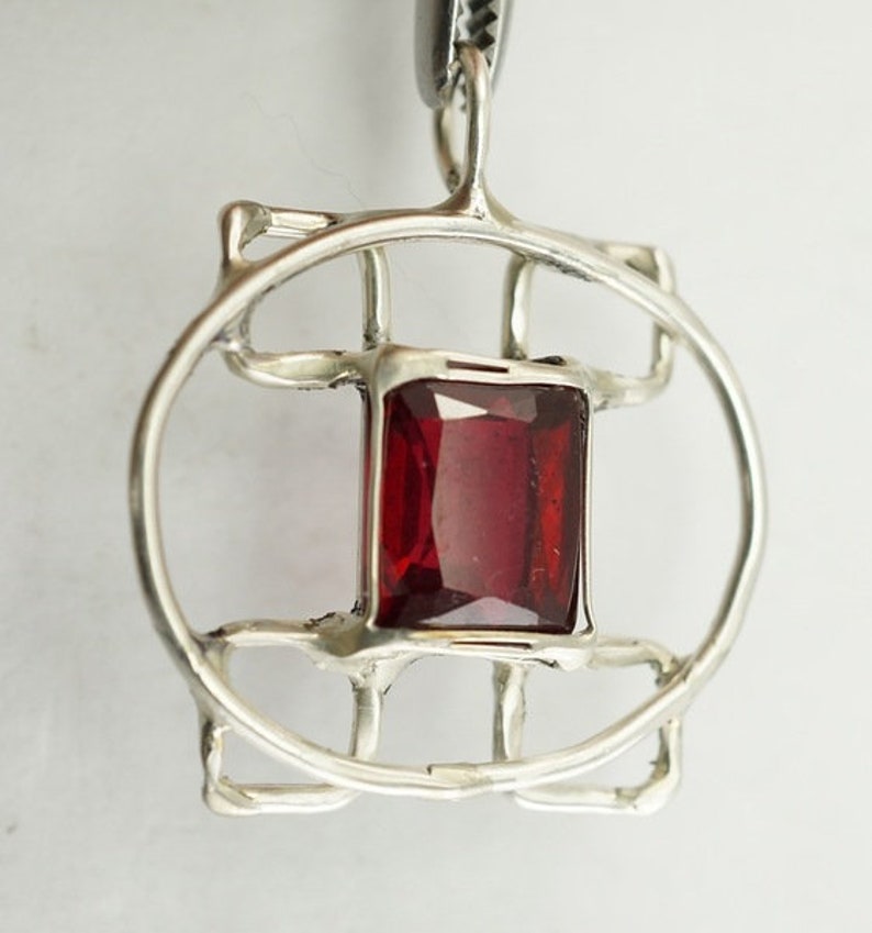 May include: A silver pendant featuring a red gemstone set within a geometric design.