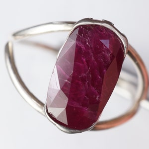 Op de afbeelding: Een zilveren ring met een grote, gefacetteerde robijn. De robijn is diep rood van kleur en heeft een licht onregelmatige vorm.