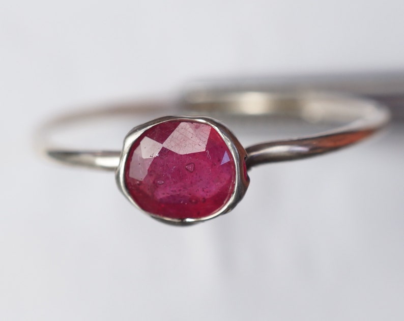 May include: A silver ring featuring a faceted ruby gemstone. The ring has a simple, delicate band and a bezel setting.