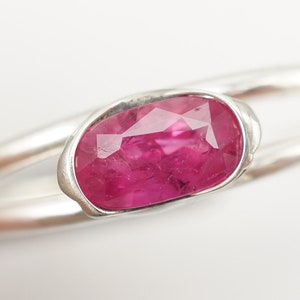 May include: A silver ring with a pink oval-shaped gemstone set in a bezel setting.