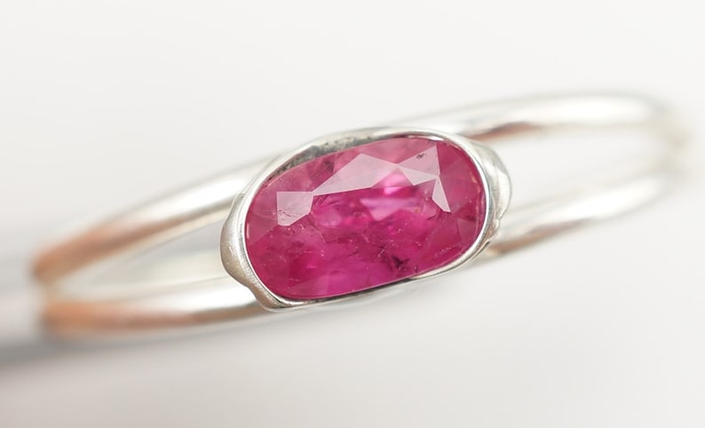 May include: A silver ring with a pink oval-shaped gemstone set in a bezel setting.