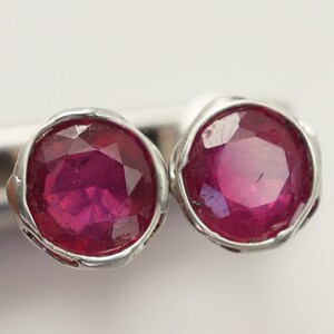 May include: A pair of silver earrings with red ruby gemstones. The rubies are round and have a faceted cut.