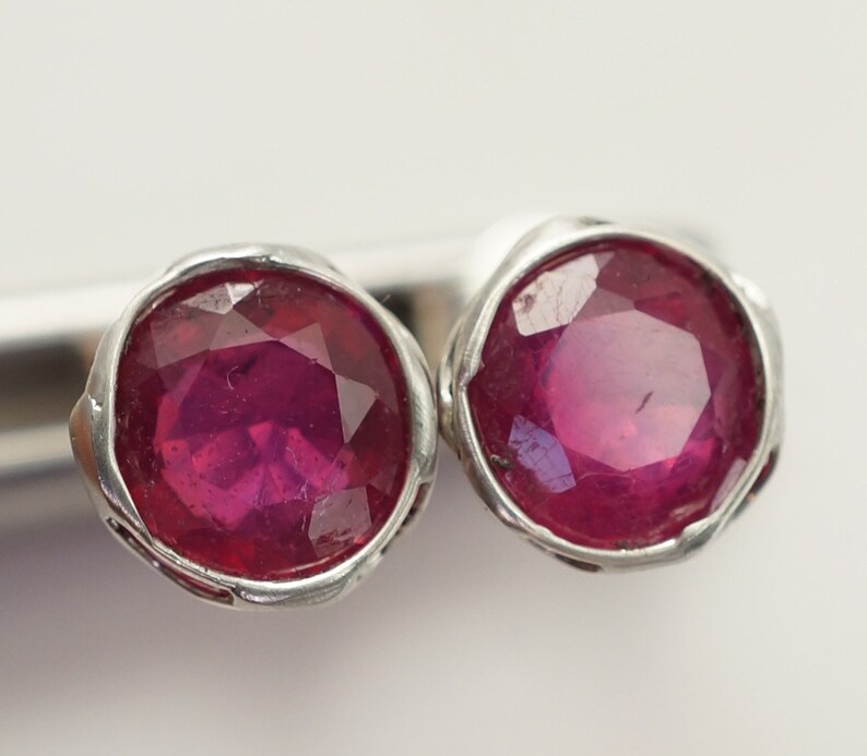 May include: A pair of silver earrings with red ruby gemstones. The rubies are round and have a faceted cut.