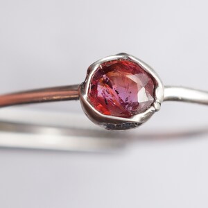 Op de afbeelding: Een zilveren ring met een roze edelsteen in een bezel-setting.