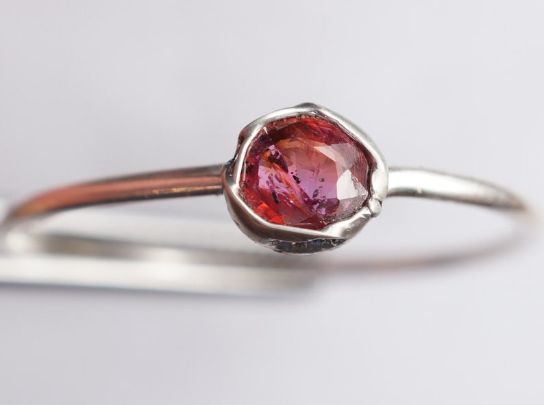 Op de afbeelding: Een zilveren ring met een roze edelsteen in een bezel-setting.