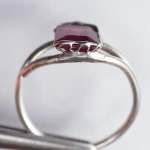 May include: A silver ring with a deep red gemstone set in a delicate, intricate design.