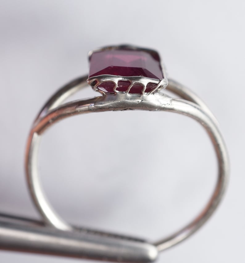 May include: A silver ring with a deep red gemstone set in a delicate, intricate design.